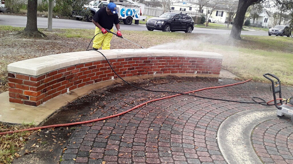 a photo of a man pressure washing a brick bench